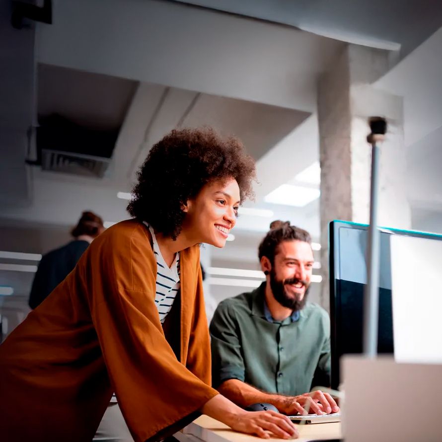 Two colleagues are happily working on a computer because their website has risen in the rankings of the main search engines.